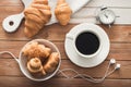 white cup of coffee with croissant, alarm clock and music headphones
