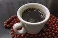 White cup of coffee on a dark surface surrounded by red beads Royalty Free Stock Photo