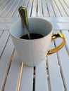 A white cup of coffee with a golden handle and a teaspoon in it