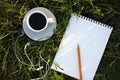 White cup of coffee, headphones, and open blank notebook on the green grass. Top view. Copy space. Summer lifestyle