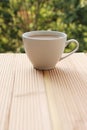 White cup with coffee on a light wooden table against a green summer garden, close-up, copy space Royalty Free Stock Photo