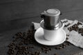 White cup of coffee with a metal filter on a top and scattered beans on a wooden table. Traditional vietnamese coffee.