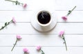 White cup of coffee with pink flower on white wooden table in the morning sunny day.