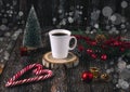 A white cup of coffee and red Christmas lollipops in the shape of a heart on a table on a dark background.