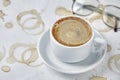 White cup of coffee on a saucer and reading glasses on a table stained with imprints of coffee cups Royalty Free Stock Photo
