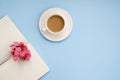 White cup of coffee silver notepad, pink flower on a blue background. Flat lay. copy space. top view