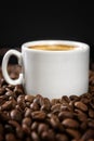 White cup of coffee with sprinkled beans. Black background. Vertical Royalty Free Stock Photo