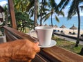 White cup of coffee stands on balcony overlooking sea and tourist