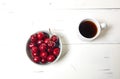 White cup with coffee and sweet cherries in a ceramic bowl on a white wooden background, closeup Royalty Free Stock Photo