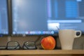 White cup of coffee or tea, glasses and a red apple on blurred background of personal computer screen Royalty Free Stock Photo