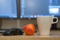White cup of coffee or tea, mouse controller and a red apple on blurred background of personal computer screen Royalty Free Stock Photo