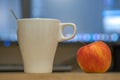 White cup of coffee or tea and a red apple on blurred background of personal computer screen Royalty Free Stock Photo