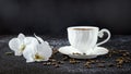 White cup of coffee, white orchid flowers, coffee beans. Romantic composition on a black background Royalty Free Stock Photo