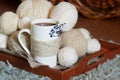 White Cup decorated with twine rope and blue dried flower and white wool threads different sizes balls on wooden tray. cozy warm Royalty Free Stock Photo