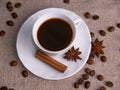 A white cup of espresso stands on a burlap table with scattered coffee beans, a cinnamon stick and stars of anise Royalty Free Stock Photo