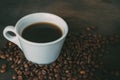 White cup filled with coffee, surrounded by coffee beans on a dark wooden background. Royalty Free Stock Photo