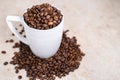 A white cup filled with roasted cinnamon coffee beans standing on brown marble surrounded by coffee beans