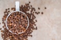 A white cup filled with roasted cinnamon coffee beans standing on brown marble surrounded by coffee beans Royalty Free Stock Photo