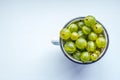 White cup Filled With Succulent Juicy Fresh Ripe Green Gooseberries On white background, Top view. Summer detoz food