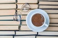 A white cup of fragrant coffee cappuccino and reading glasses against the background of worn old books stacked upside Royalty Free Stock Photo