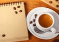 White Cup of fragrant espresso coffee with foam and writing pad, scattered coffee beans on a wooden table, copy space Royalty Free Stock Photo