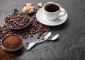 White cup of fresh raw organic coffee with beans and ground powder with cane sugar cubes with coffee tree leaf on black background