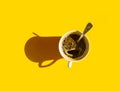 White cup of freshly brewed coffee with foamy crema tea spoon on solid yellow background. Top view. Morning breakfast energy Royalty Free Stock Photo