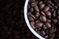 White cup full of coffee beans close up against the coffee beans background. Coffee mug. Royalty Free Stock Photo