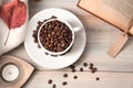 A white Cup full of coffee beans on a light beige wooden background with a book and a sweater. Royalty Free Stock Photo