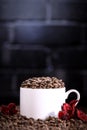 White cup full of coffee beans , red flowers and red chocolate candy against the background of a dark brick wall. Morning espresso Royalty Free Stock Photo