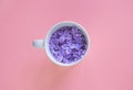 White cup full of lilac flowers on the pink background