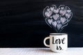 White cup with hand lettering text LOVE IS and chalk-drawn small Royalty Free Stock Photo