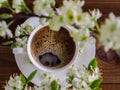 A white cup of hot aromatic coffee and branch of a blossoming cherry tree on a wooden background. Flat layout. View from Royalty Free Stock Photo