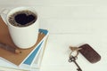 White cup of hot black coffee with fresh bubble in heart shape on book stack decorated with pencil and vintage key on white wooden