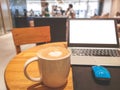 A white cup hot capuccino with white heart mug on top, a white screen computer labtop and blue mouse on brown wooden table Royalty Free Stock Photo