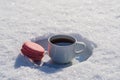 White cup of hot coffee with pink macaroon on a bed of snow and white background close up