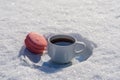 White cup of hot coffee with pink macaroon on a bed of snow and white background, close up