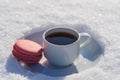 White cup of hot coffee with pink macaroon on a bed of snow and white background, close up