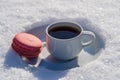 White cup of hot coffee with pink macaroon on a bed of snow and white background, close up