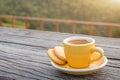 A white cup of hot espresso coffee mugs placed with cookies on a wooden floor with morning fog and moutains with sunlight Royalty Free Stock Photo