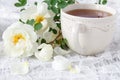 White Cup of hot herbal tea. Vintage tablecloth. Branches of wild rose