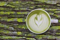 White cup of matcha green tea latte art with foam on rustic moss wooden table with copy space