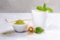 White cup with matcha green tea, powder with special wooden spoon, bamboo whisk, fresh leaves on grey backdrop. Royalty Free Stock Photo