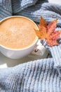 White cup of morning warming coffee on blue knitted sweater with maple yellow leaves background. Cozy home concept