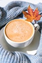 White cup of morning warming coffee on blue knitted sweater with maple yellow leaves background. Cozy home concept