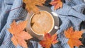 White cup of morning warming coffee on blue knitted sweater with maple yellow leaves background. Cozy home concept