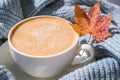 White cup of morning warming coffee on blue knitted sweater with maple yellow leaves background. Cozy home concept