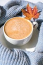 White cup of morning warming coffee on blue knitted sweater with maple yellow leaves background. Cozy home concept