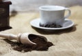 White cup and plate with beans, milling coffee and a wooden grinder on rustic background Royalty Free Stock Photo