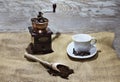 White cup and plate with beans, milling coffee and a wooden grinder on rustic background Royalty Free Stock Photo